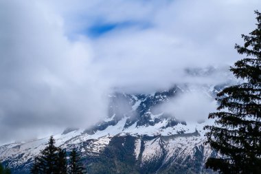 Aiguille de Blaitiere 'in karla kaplı yamaçları yoğun bulutlarla örtülmüş. Fransız Alpleri' ndeki dramatik manzarayı çevreleyen yeşil ağaçlar..