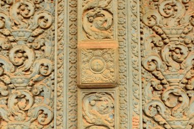 Çiçek ve parşömen motifleriyle süslenmiş kumtaşı oymaları Angkor, Kamboçya yakınlarındaki Baksei Chamkrong tapınağının antik duvarını süslüyor. Karmaşık desenler ve yıpranmış yüzey yumuşak gün ışığıyla vurgulanır, tarihi Khmer 'i gözler önüne serer.