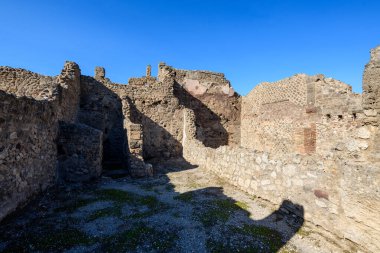 Antik volkanik taş ve tuğla duvarlar İtalya 'nın Pompeii bölgesinde açık bir avlu oluşturur. Parlak güneş ışığı, bu tarihi yüzeyin dokularını ve yıpranmış yüzeylerini vurgulayarak, pürüzsüz duvarlar üzerinde keskin gölgeler oluşturur.