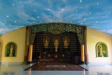 Üç altın Buda heykeli, karmaşık altın kemer detaylarıyla çerçevelenmiş, koyu ahşap bir sunakta otururlar. Boyalı bir gökyüzü tavanı ve parlak zeminleri vardır. Neşeli, huzurlu bir tapınak ortamı yaratırlar..