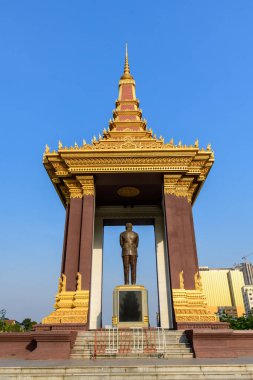 Karmaşık Khmer mimari detaylarıyla süslü altın pavyon Phnom Penh, Kamboçya 'da açık mavi bir gökyüzünün altında duruyor. Yapı, dekoratif altın aksanları ve geometrik çizgileriyle çarpıcı bir kent simgesi oluşturan bronz bir heykeli barındırıyor..