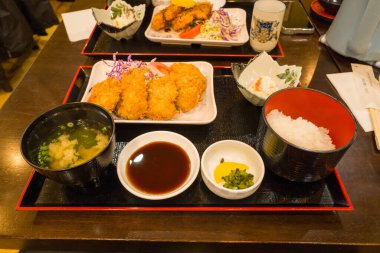 Klasik Japon sofrası: çıtır ekmek arası pirzola, buharda pişirilmiş beyaz pirinç, miso çorbası, turşu, sos ve taze salata. Hepsi de ılık restoran aydınlatmasında sunuluyor..