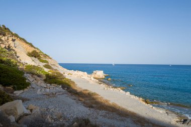 Sakin, taştan bir kıyı şeridi Porto Giunco yakınlarında canlı mavi Akdeniz ile buluşuyor engebeli uçurumlar ve bulutsuz bir gökyüzünün altında seyrek bir bitki örtüsü..