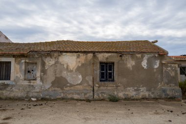 Sardinya 'nın terk edilmiş Asinara Ulusal Parkı' ndaki bulutlu bir gökyüzünün altında kırık duvarları ve parmaklıklı camları olan terk edilmiş bir bina duruyor. Soluk dokular ve soluk renkler terk edilmişlik ve yalnızlık hissi uyandırıyor..