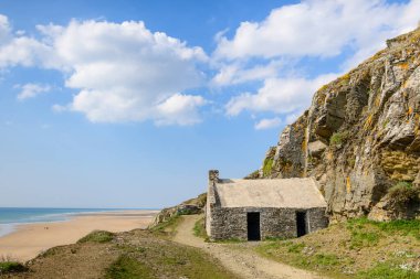Yıpranmış uçurumların dibinde uzanan taştan bir bina geniş kumlu bir sahile ve Cap de Carteret 'te sakin bir denize bakıyor. Parlak güneş ışığı ve mavi gökyüzü sakin, davetkar bir sahil manzarası yaratır..