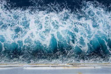Akdeniz 'de hareket halindeki bir teknenin arkasında köpükle çalkalanan canlı turkuaz suyun havadan görünüşü. Dinamik dokular ve dönen şekiller enerjik bir deniz manzarası yaratır..