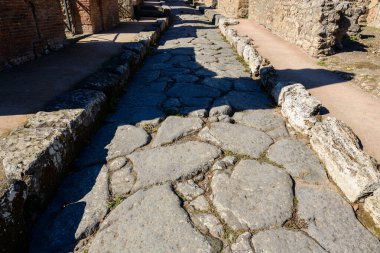 Pompeii arkeoloji sahasındaki bir Roma caddesinde yıpranmış volkanik taş döşemesinin ayrıntılı görüntüsü. Kaba dokular ve düzensiz şekiller güneş ışığıyla vurgulanır ve bu antik şehrin tarihi işçiliğini gözler önüne serer..