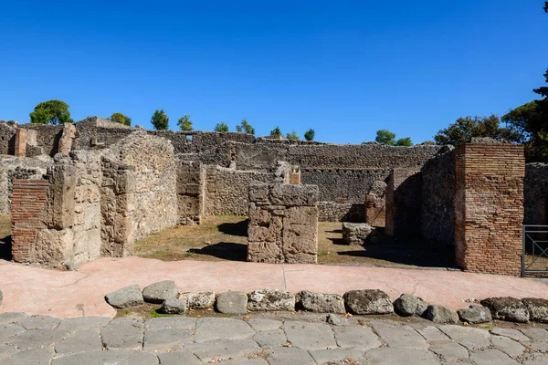 Yıpranmış volkanik taş ve tuğla duvarlar İtalya 'nın Pompeii kentindeki arkeoloji sahasında canlı bir mavi gökyüzünün altında duruyor. Sahne, pürüzlü duvarcılık, açık alanlar ve bu antik Roma şehrinin tarihi dokularını vurguluyor..