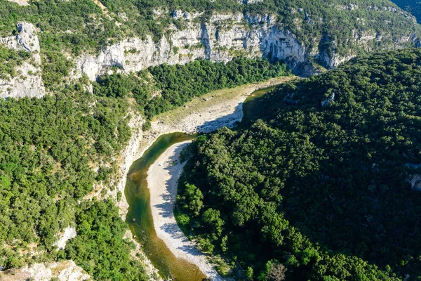 Dik kireçtaşı kayalıklarının tabanını izleyen kıvrımlı bir nehrin hava perspektifi Gorges de Ardeche 'de yoğun yeşil ormanla kaplıdır. Parlak güneş ışığı kayalık araziyi ve yemyeşil örtüyü aydınlatır. Güçlü zıtlıklar ve canlı renkler yaratır..
