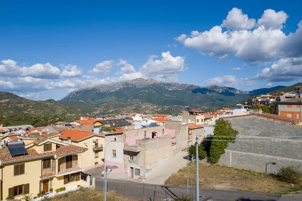 Sardunya 'nın aydınlık günışığında engebeli dağları ve arka planda dağınık bulutları olan Orgosolo şehrinin renkli çatıları..