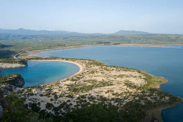 Voidokilia Sahilleri 'nin ikonik hilal çubuğu ve sakin mavi lagünün hava manzarası. Messenia, Peloponnese' deki alçak kum tepeleri ve yemyeşil Akdeniz bitkileriyle çevrili..