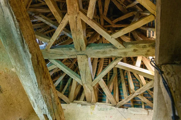 Karmaşık ahşap kirişler tarihi bir kilisenin çatısının altında karmaşık bir geometrik desen oluşturur. Yıpranmış kirişler ve korunmasız yapı geleneksel işçiliği ve eski kerestelerin dokulu yüzeylerini vurguluyor.