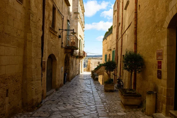 İtalya 'nın Matera kentindeki yıpranmış taş binalar arasında sakin bir kaldırım taşı sokak rüzgarı, sıcak güneş ışığı ve saksı yeşilliği ile tarihi mekana cazibe katıyor..