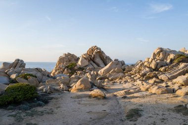 Güneşli granit kayalar ve kayalar Sardunya 'daki Capo Testa kıyı şeridi boyunca dramatik şekiller yaratırken, arka planda sakin Akdeniz berrak bir gökyüzünün altında.