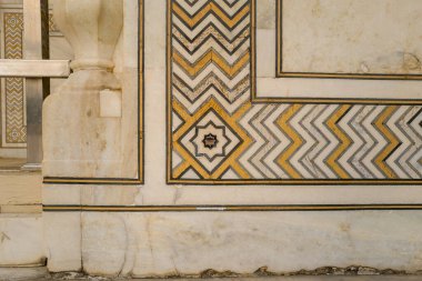 Agra 'daki Tac Mahal mozolesinin alt duvarında altın ve siyah aksanlı yıldız şekilli mermer kaplama. Geometrik desenler ve cilalanmış taş yüzey yumuşak gün ışığıyla aydınlatılır..