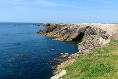 Dik kayalıklar, Saint Pierre Quiberon 'daki Pointe Beg-An-Aud' daki berrak mavi suların üzerinde canlı yeşil çimenler ve güneşli bir gökyüzünün altında kır çiçekleriyle yükseliyor..