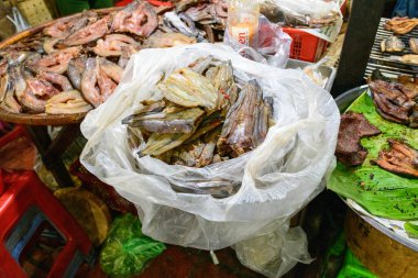 Kamboçya 'nın Phnom Penh kentindeki pazarda çeşitli kurutulmuş balıklar plastik bir poşette ve tepsilerde sergileniyor. Sahnede kırsal dokular, doğal renkler ve yerel gıda kültürünün bir kısmı yer alıyor..