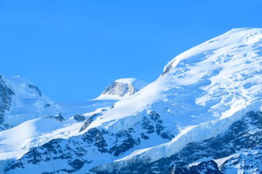 Parlak güneş ışığı, Mont Blanc kalabalığındaki parlak mavi gökyüzünün altında Grand Pilier Dörtgeninin el değmemiş, karla kaplı yamaçlarını ve engebeli buz oluşumlarını vurgular..