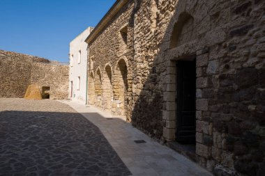 Castelsardo 'daki tarihi avluda dokulu taş duvarlar, kemerli kapılar ve berrak mavi gökyüzünün altında güneşli kaldırımlar var..