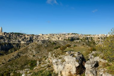 Matera, İtalya 'nın geniş manzarası, engebeli uçurumların tepesine tünemiş antik taş binaları ve berrak gökyüzünün altında güneşli kayalık bir vadi..