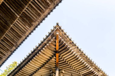 Ahşap tapınak çatılarının kesiştiği açısal manzara, Japonya 'nın Himeji kentindeki Engyoji Dağı' nda soluk mavi gökyüzüne çarpıcı bir geometrik desen oluşturur. Doğal ahşap dokular ve simetri parlak gün ışığıyla vurgulanır.