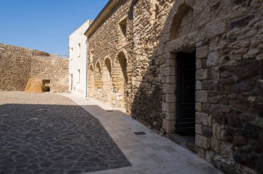 Castelsardo, Sardinya 'nın tarihi merkezinde engebeli taş duvarları ve kemerli kapıları olan güneşli avlu, zamansız Akdeniz cazibesini çağrıştırıyor..