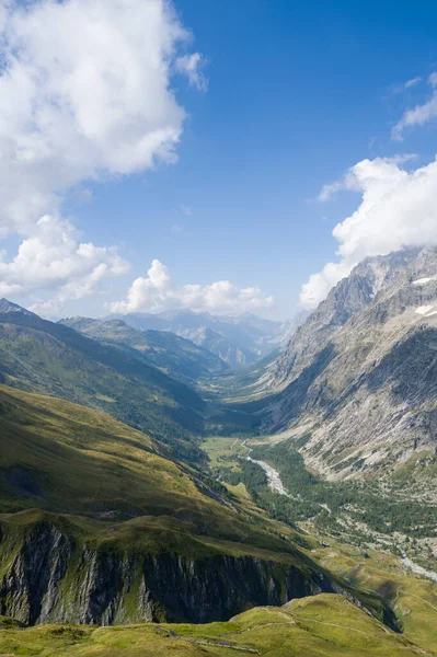 Val Ferret 'in yüksek açılı manzarası yemyeşil bir vadi, dramatik dağ tepeleri ve dağınık beyaz bulutlu mavi gökyüzünün altında dolambaçlı bir nehir gösteriyor..