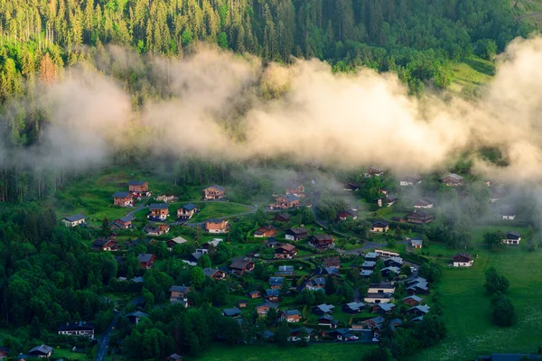 Alçak bulutlar, Les Houches 'da gündoğumunda yemyeşil ormanlarla çevrili geleneksel dağ kümelerinin üzerinde sürüklenerek barışçıl ve atmosferik bir dağ manzarası oluşturur..