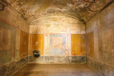 Aşıklar Evi, Pompeii, İtalya 'da soluk geometrik fresklerle solmuş mavi ve kırmızı tonlu antik kubbeli oda duruyor. Yıpranmış alçı ve ince renk izleri, yumuşak ve dağınık ışığın altında Roma 'nın tarihi iç kısımlarını ortaya koyuyor..
