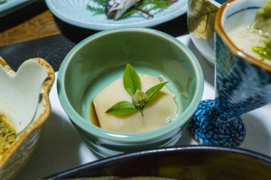 Soluk yeşil bir seramik kasede taze bir yaprak ve wasabi ile kaplı pürüzsüz bir tofu bloğu servis edilir. Düzenleme, diğer Japon yemekleri arasında hafif ışıklandırma ve rafine edilmiş minimalist bir sunum içermektedir..