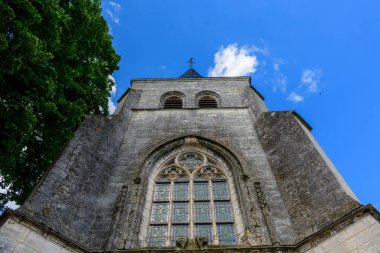 Pouilly sur Loire 'da canlı bir mavi gökyüzüne karşı kurulmuş süslü kemerli cam pencere ve çan kulesinin yer aldığı tarihi bir kilise cephesinin alçak açılı görüntüsü. Yıpranmış duvarcılık ve karmaşık traktör kalıtım ve zamansızlığı çağrıştırıyor..