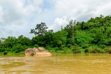 Çamurlu Nam Ou Nehri 'nden çıkan büyük bir kaya, Laos' un kuzeyinde yer alan Muang Ngoi yakınlarındaki yoğun yeşil orman ve tepenin üzerine kurulmuştur. Sahnede canlı yapraklar ve parçalı bulutlu bir gökyüzü var. Nehrin doğal dokusunu vurguluyorlar.