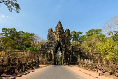 Kamboçya 'nın Siem Reap kenti yakınlarındaki Angkor Thom' un ikonik güney kapısına geniş bir cephe manzarası. Antik Khmer geçidi, sıcacık tropikal ormanın ortasında duruyor.