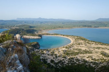 Hilal koyunu, altın kumu ve sakin mavi lagünü silip süpüren Voidokilia Sahilleri 'nin geniş perspektifi Messenia, Mora' daki engebeli tepeler ve Akdeniz bitkileriyle çevrili..