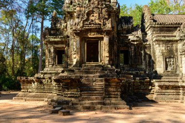 Thommanon Tapınağı 'nın zengin kumtaşı girişi eski yapıya giden derin gölgeler ve dokulu adımlarla kıtır kıtır güneş ışığıyla aydınlanıyor. Uzun orman ağaçlarıyla çevrelenen sahne, ayrıntılı rahatlamaları vurguluyor ve