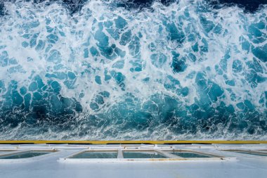 Akdeniz 'de hareket eden bir geminin ardından köpüklü turkuaz suyun çalkantılı görüntüsü. Gemi güvertesi ve girdap okyanusu arasındaki keskin dokular ve canlı kontrastlar dinamik bir deniz soyutlaması yaratır..