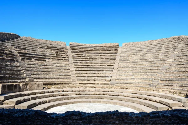Kıvrımlı taş koltuklar Pompeii, İtalya 'daki küçük tiyatronun yarı dairesel amfitiyatrosunu oluşturur. Parlak güneş ışığı, canlı mavi gökyüzünün altındaki basamağın geometrik çizgilerini vurgular..