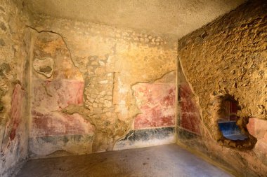 İtalya, Pompei 'deki Aşıklar Evi' nde soluk kırmızı duvar resimleri, açıkta duran volkanik taşlar ve alçıda büyük bir delik bulunan eski bir oda. Ilık ışık desenli duvar işçiliğini ve Roma iç dekorasyonunun izlerini ortaya çıkarıyor..