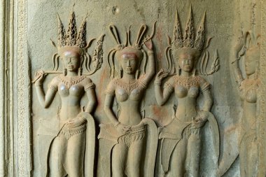 Üç apsara dansçısının karmaşık taş oyması Angkor Vat 'taki onur terasını süslü başlıklar ve yumuşak doğal ışıkla renklendirilmiş takılarla süslüyor. Dokulu kumtaşı yüzeyi ve çiçek desenleri sanatsal