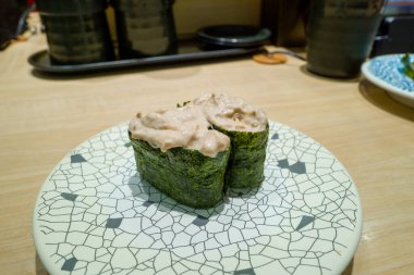 Çağdaş bir Osaka suşi restoranının açık ahşap tezgahının tepesinde beyaz bir tabağa sarılı kurutulmuş ton balığı salatası Gunkan suşisi servis edilir..