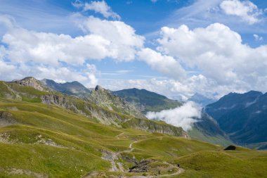 Dolaşan bir yürüyüş yolu yeşil tepeler yuvarlanan kayalık tepeler dramatik dağ tepeleri altında ve Fransız Alplerinde dalgalanan bulutlarla dolu bir gökyüzü..