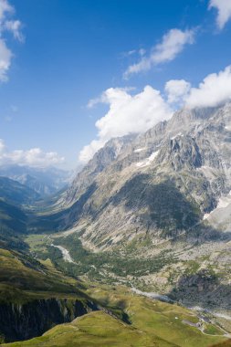 Val Ferret 'in engebeli tepeleri, yemyeşil yamaçları ve dağınık bulutlu mavi gökyüzünün altında dolambaçlı bir nehri süpüren hava manzarası..