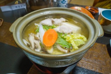Haşlanmış tavuk, tofu, mantar, Napa lahanası ve havuç dilimlenmiş temiz et suyuyla dolu bir köy çömleği. Tabak ahşap bir masada sunuluyor. Geleneksel bir Japon ortamında taze malzemeler ve rahatlatıcı dokular sergileniyor..