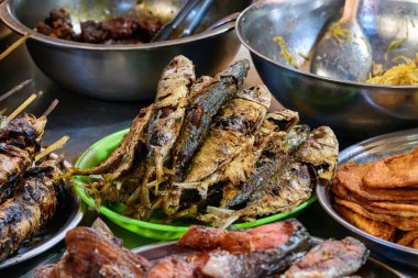 Kamboçya, Kamboçya 'da bir lokantada ızgara et ve balık köfteleriyle çevrili çeşitli kızarmış balıklar, yeşil bir tabakta istiflenir. Görüntü, geleneksel Güneydoğu Asya sokak yemeklerinin gevrek dokularını ve canlı renklerini vurguluyor.