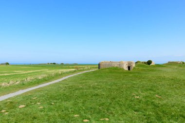 Tarihsel beton sığınak Normandiya 'nın Longues-sur-Mer kentinde denize bakan yeşil bir burunda duruyor. Açık arazi ve açık mavi gökyüzü dingin ve geniş bir atmosfer yaratır..