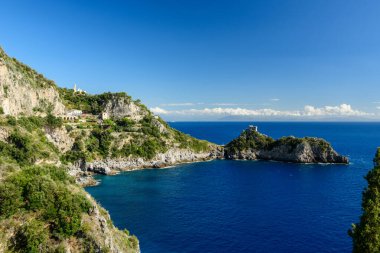 Güneşli kayalık kayalıklar ve yemyeşil Akdeniz bitki örtüsü İtalya 'nın Capo di Conca bölgesindeki tarihi gözlem kulesini çevreledi. Amalfi Sahili 'nin derin mavi suları canlı bir gökyüzünün altında dramatik kıyı manzarasını vurguluyor..