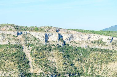 Navacelles Sirki 'nde açık mavi gökyüzünün altında, engebeli dokuları ve yeşil bitki örtüleriyle aydınlık kireçtaşı sırtı bulunuyor. Manzara açık, vahşi ve doğal olarak canlı..