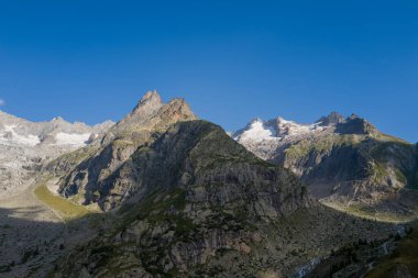 Engebeli bir vadiden yükselen buzullar ve karla kaplı yüksek kayalık tepe. Mont Blanc 'ın parlak mavi gökyüzünün altında aydınlık bir öğleden sonra ışığı altında..