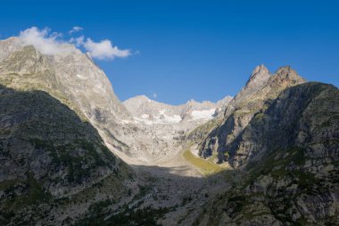 Dik, kayalık yamaçlar ve engebeli tepeler arasında uzanan geniş bir dağ havzası. Derin mavi bir gökyüzünün altında, parlak güneş ışığıyla aydınlatılıyor..
