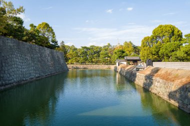 Japonya 'nın Kyoto kentindeki Nijo Kalesi' nde mavi gökyüzü altında geleneksel kapı mimarisine sahip heybetli taş duvarlar ve yemyeşil ağaçlarla çevrili geniş hendek..